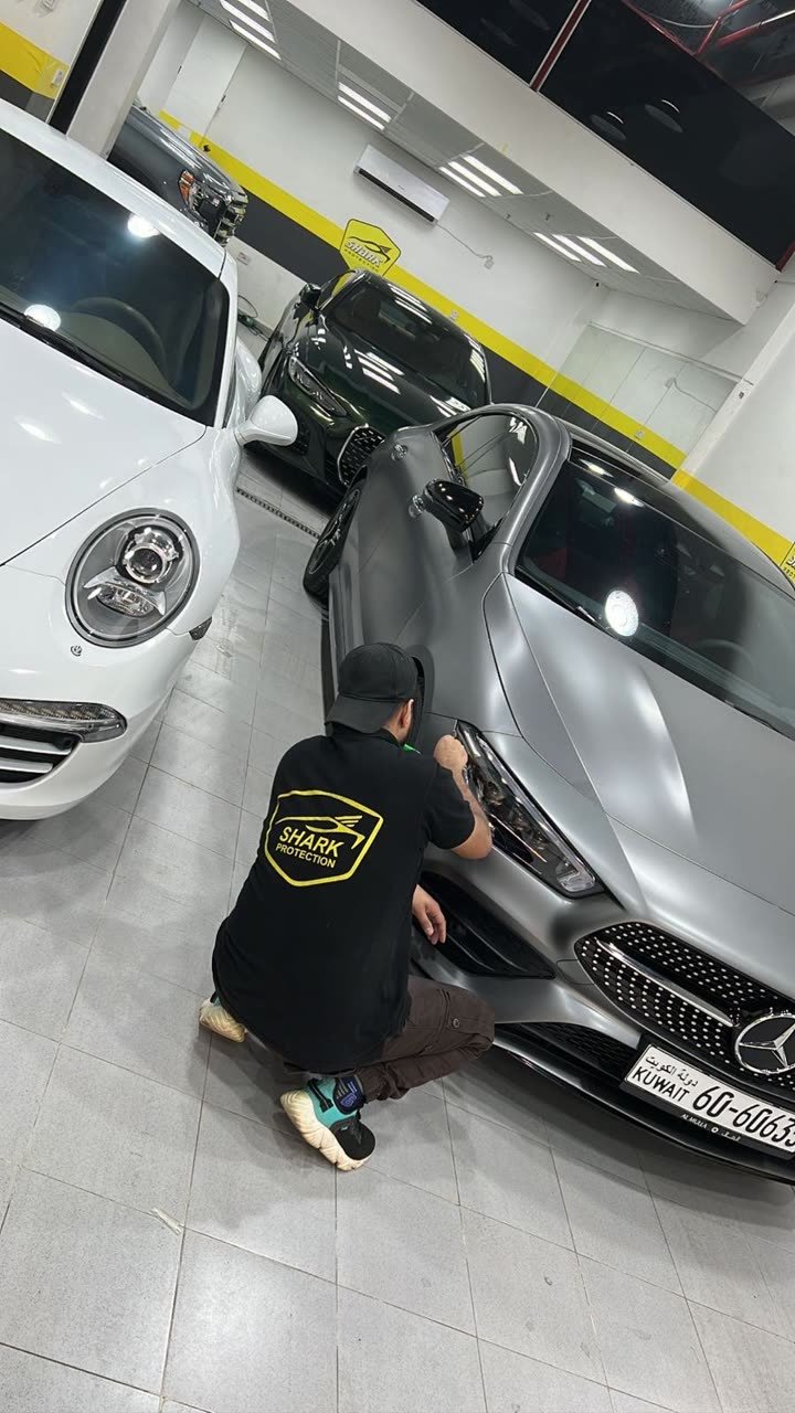 Work on a matte Mercedes beside a white Porsche